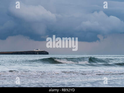 Der Leuchtturm auf Farne Islands vom Strand von Bamburgh, Northumberland, England, Großbritannien, nach Sonnenuntergang in der Dämmerung mit dem Meer und Wellen. Stockfoto