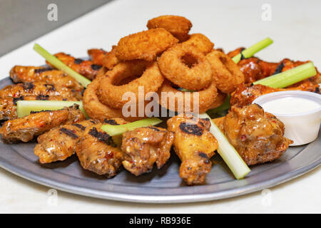 Das Essen in der Bar: Chicken Wing Platte mit Zwiebeln und Sellerie. Behälter mit weißer Soße auf dem Whiteboard. Seitenansicht hautnah. Stockfoto