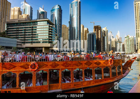 Dubai, VAE 11. 10. 2018: die berühmte traditionelle Holz- alten Dhow Cruise tour in der Marina mit Touristen auf dem Board und moderne Wolkenkratzer in der backgou Stockfoto