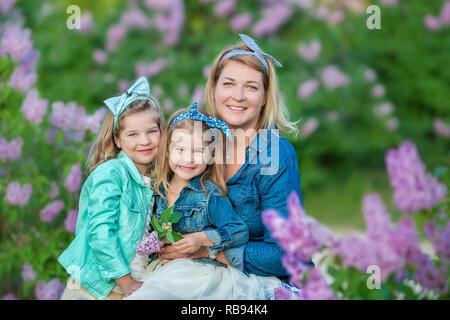 Mutter Frau mit zwei nett lächelnden Mädchen Schwestern gemeinsam schön auf einem lila Feld Bush alle tragen elegante Kleider und Mäntel Jeans Stockfoto