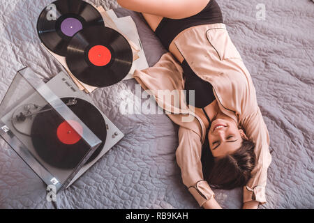 Hohe Betrachtungswinkel von Mädchen mit auf dem Bett und höre Vinyl Audio Player zu Hause Stockfoto