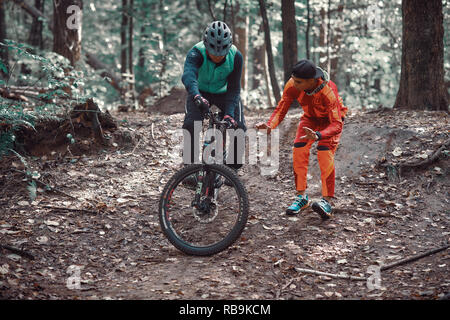 Moskau, Russland - Nov, 2018: MTB-Lehrer helfen Reiter lernen, Fahrrad zu fahren. Lehre ein Reiter, ein Fahrrad auf einem Trail zu fahren. Zwei Freunde haben Spaß in der Natu Stockfoto