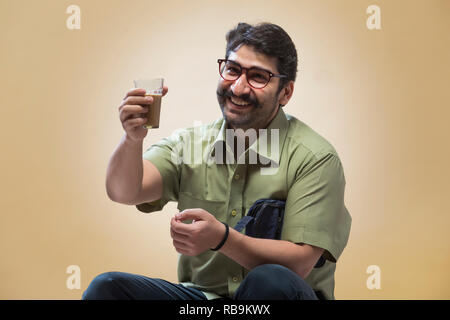Lächelnder Mann mit Brille mit einer kleinen Tasche und suchen bei einem Glas Tee in der Hand. Stockfoto