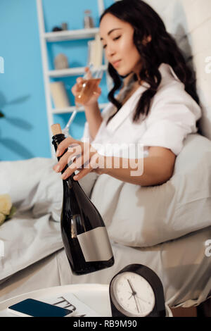 Schöne junge asiatische Frau mit Flasche Wein trinken und im Bett Stockfoto