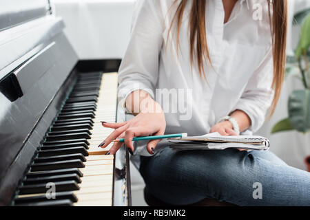 7/8-Ansicht von Mädchen im weißen Hemd mit Notebook Klavier spielen und Komponieren von Musik zu Hause. Stockfoto