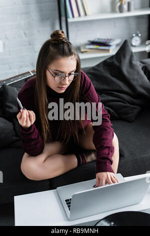 Attraktives Mädchen sitzen auf der Couch und hält Marihuana gemeinsame und mit Laptop im Wohnzimmer Stockfoto