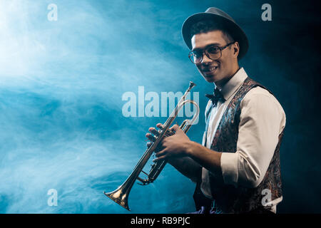 Lächelnd männlichen Musiker mit Trompete auf der Bühne mit dramatischen Licht und Rauch posing Stockfoto