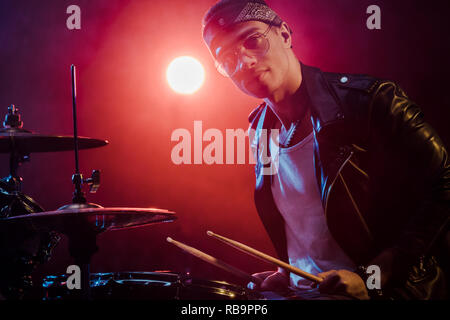 Stattliche männliche Musiker in Lederjacke Schlagzeug spielen bei Rockkonzert auf der Bühne Stockfoto