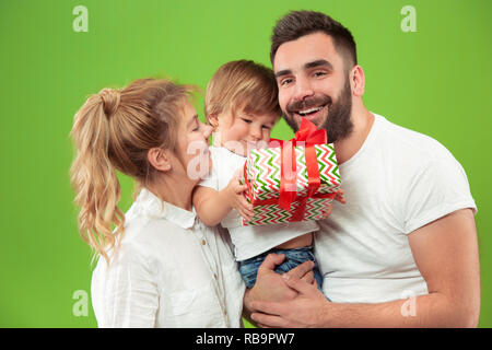 Die glückliche Familie mit Kind zusammen Posieren auf Green Studio Hintergrund. Die Menschen, das Miteinander, die Kindheit, Eltern, Liebe und Lifestyle Konzept Stockfoto