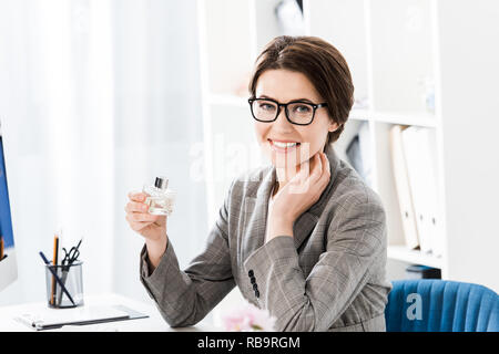 Lächelnd attraktive Geschäftsfrau Holding jar von Parfüm im Büro und suchen an Kamera Stockfoto