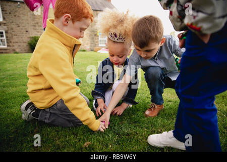 Gruppe junger Kinder kniete in einem Kreis im Freien zu verteilen der Ostereier, die sie gefunden haben. Stockfoto