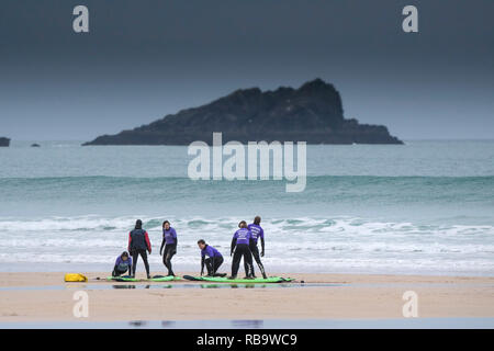 Eine Gruppe von unerfahrenen Surfer mit einer surflektion auf Fistral Beach mit der felsigen Insel namens Die Gans im Hintergrund. Newquay Cornwall. Stockfoto