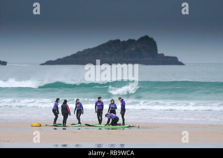 Eine Gruppe von unerfahrenen Surfer mit einer surflektion auf Fistral Beach mit der felsigen Insel namens Die Gans im Hintergrund. Newquay Cornwall. Stockfoto