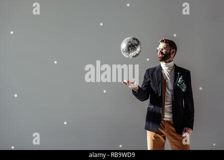 Schöner Mann in Gläsern werfen bis Disco ball auf grauem Hintergrund Stockfoto