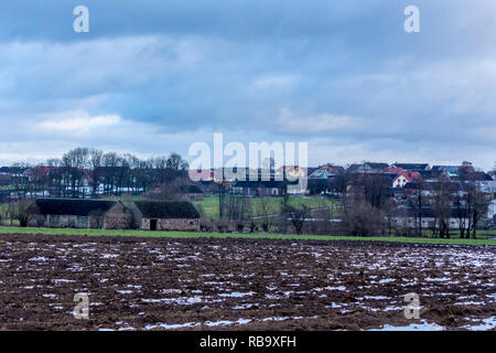 Ein wenig Schnee an den Furchen des Feldes. Dorf und die Bäume im Hintergrund. Beginn des Winters in Europa. Stockfoto