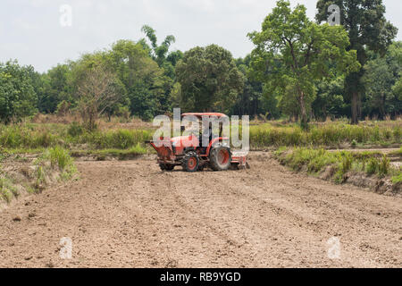 Thailändische Bauern sind mit einem Traktor der Boden für den Anbau von Reis vorzubereiten. Stockfoto