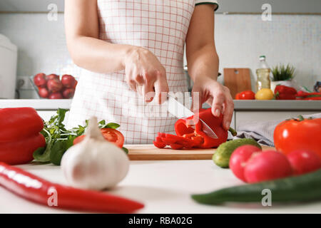 Hausmannskost. Eine Frau in der Küche Schnitte Red Paprika auf einem Holzbrett. Gesunde, frische Lebensmittel Stockfoto
