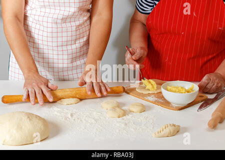 Die Familie kocht gemeinsam in der Küche, close-up. Ältere Frau im roten Küche Schürze formt Kuchen und erwachsene Tochter rolling Teig mit einem rollenden Stockfoto