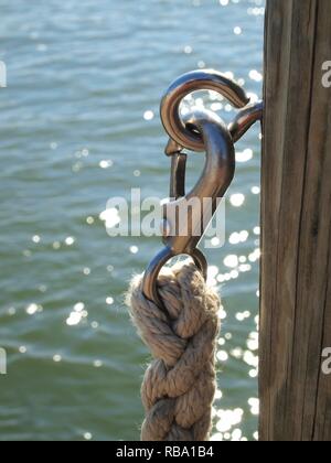 Geflochtenes nautisches Seil und Metallclip auf hölzerner Dock Post. Vertikales Bild mit Minimalismus, Farbe und Texturen. Blick vom Dock auf Kent Island i Maryland Stockfoto