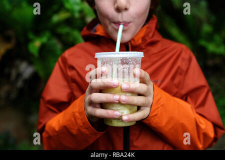 Nahaufnahme der kaukasischen boy Holding eine Schale aus Kunststoff mit beiden Händen und Trinken tropischen Saft mit Strohhalm Stockfoto