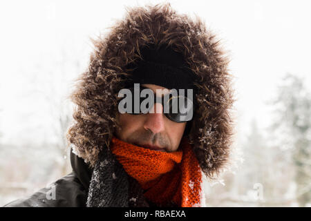 Porträt von einem einzigen männlichen winter Abenteurer das Tragen eines warmen grünen Mantel mit Fell Kapuze, einen blauen ski Mütze, Schal und eine Orange Schwarz retro style Schutzbrille Stockfoto