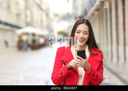 Vorderansicht eines glücklichen Frau in Rot Walking mit Smart Phone auf der Straße im Winter Stockfoto