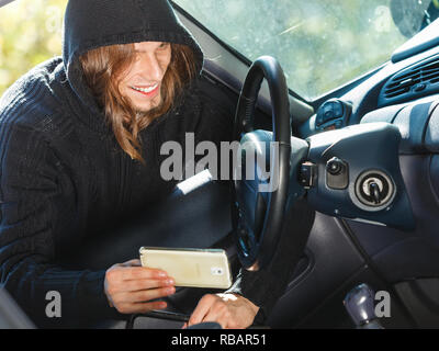 Anti Theft system problem Konzept. Einbrecher, Dieb Mann mit schwarzer Kleidung brechen in Auto und stehlen Smartphone Stockfoto