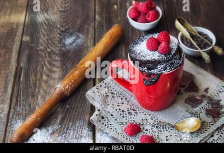 Frische hausgemachte Schokolade Kuchen in Becher auf rustikalen Holzmöbeln Hintergrund. In der Mikrowelle zubereitet. Stockfoto