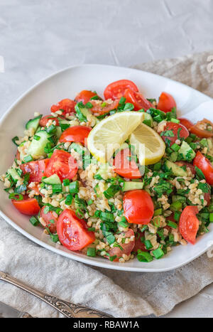 Tabbouleh (Tabouli) Salat auf einem Teller auf Hellgrau konkreten Hintergrund. Gesunde vegetarische Nahrung. Libanesische Küche. Selektive konzentrieren. Stockfoto