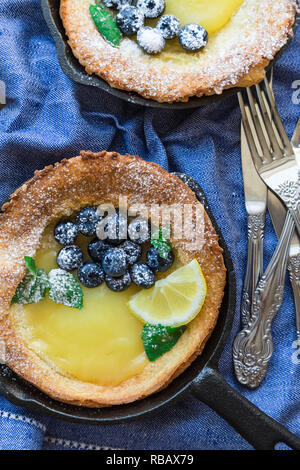 Frische hausgemachte Niederländische Baby Pfannkuchen mit Zitronen Quark und Blaubeeren in Eisen skillets. Ansicht von oben. Stockfoto