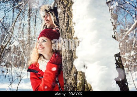 Verspieltes Paar versteckt sich hinter einen Baum im Schnee Stockfoto