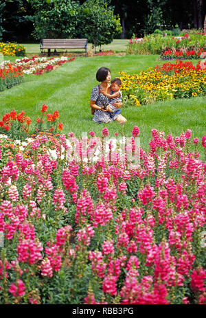 Eine asiatische Frau hält Ihr kleines Kind beim Sitzen inmitten einer Wiese mit Blumen in einem Park in Rapid City, South Dakota Stockfoto