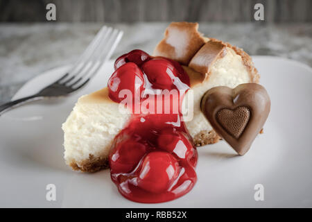 New York style Käsekuchen mit Kirschen und Schokolade Herz auf weißem Schild. Gabel im Hintergrund. Stockfoto