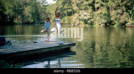 Teenage Mädchen und ihre junge Schwester Üben Yoga am Ende einer Anlegestelle. Stockfoto