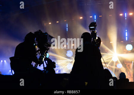 Fernsehen von einem Kameramann bei einem Konzert. Kamera mit dem Operator ist auf der Plattform. Silhouetten auf dem Hintergrund der bunte Strahl Stockfoto