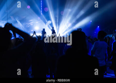 Silhouetten von einem Konzert Masse und Kameramann vor dem Hintergrund der hellen, farbigen Strahlen auf die Bühne. Kamera mit dem Operator ist auf der Pla Stockfoto