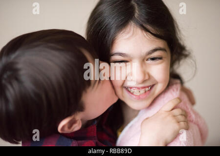 Süße kleine kaukasischen Jungen küssen fröhlich lachenden kleinen Mädchen mit Halterung Stockfoto