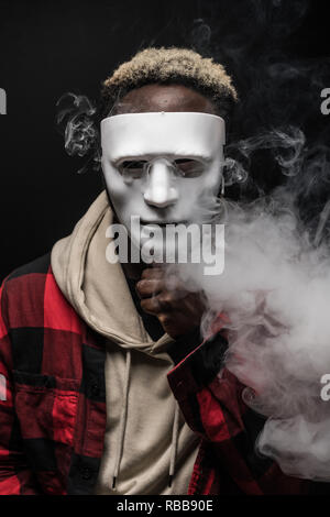 Junge afrikanische Mann mit Maske auf Gesicht vape Elektronische Zigarette Cloud mit einem Mod, Rauch Tricks der vaping Gerät Hintergrund. Stockfoto