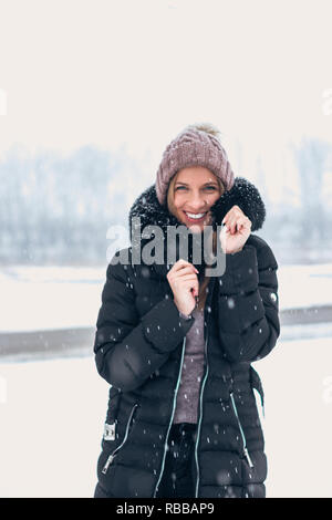 Lächelnde Frau in kaltem Wetter, während Schnee fallen. Stockfoto