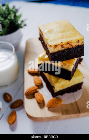 Ein Stapel von Schokolade Käse Kuchen brownies auf Holzuntergrund mit Mandeln Saatgut und Milch. Nach oben Schließen Stockfoto