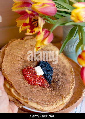 Pfannkuchen für die traditionellen russischen Frühling Urlaub. Dünne Pfannkuchen mit roter und schwarzer Kaviar und einen Strauß mit frischen Tulpen. Holz- Hintergrund und fest Stockfoto