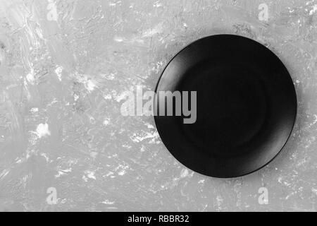 Blick von oben auf die Matte runde leeren dunklen Teller auf dunklen Zement Hintergrund Platz für Sie entwerfen. Stockfoto