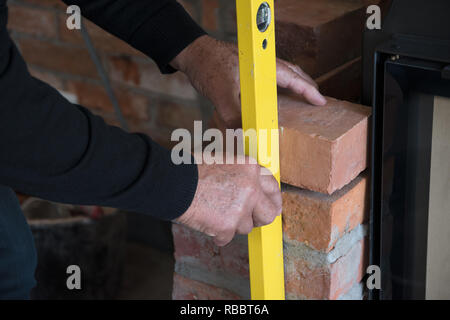 Mason überprüft ein Ziegelstein für eine Wand mit einer Wasserwaage auf einer Baustelle, ausgewählte konzentrieren Stockfoto