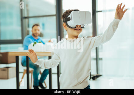 Smart Junge. Progressive kid Gefühl froh beim Tragen eines virtuellen Realität gerät und lächelnd konzentriert Stockfoto