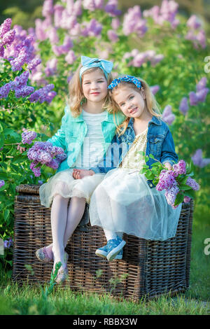 Zwei nette lächelnde Mädchen Schwestern schön zusammen auf einem lila Feld Bush alle tragen elegante Kleider und Mäntel Jeans Stockfoto