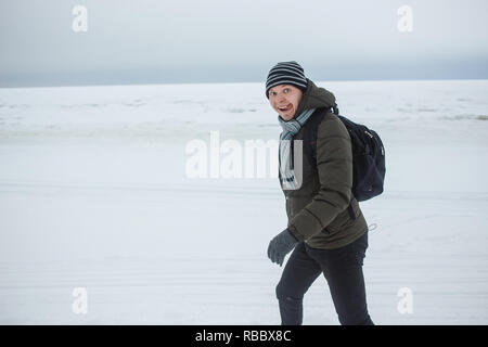 Fröhliche kaukasischen Mann Wandern auf Meer Küste Schnee bedeckt. Er zeigt lustiges Gesicht Ausdruck mit seiner Zunge heraus hängen Winter Spaß, Urlaub, gesunden Lebensstil Konzept. Stockfoto