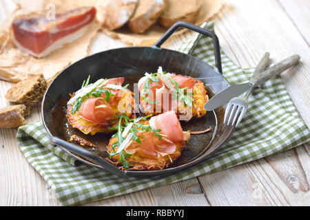 Kartoffelrösti mit Südtiroler Speck, Parmesan und Rucola Salat in eine eiserne Pfanne Stockfoto