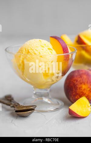 Eis mit Pfirsichen in cups auf konkreten Hintergrund. Lecker Sommer erfrischenden Dessert. Obst Eis Schaufeln Stockfoto
