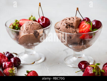 Schokolade Eis Schaufeln in transparenten Cups mit frischen Kirschen und Erdbeeren. Lecker Frisches Dessert Stockfoto