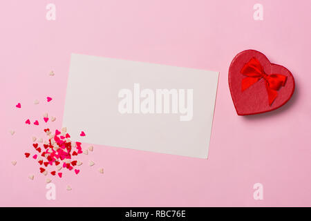 Vorhanden oder Geschenkbox, Herz aus Papier und Konfetti auf rosa Hintergrund der Ansicht von oben. Valentinstag Grusskarten. Flach Stil. Stockfoto